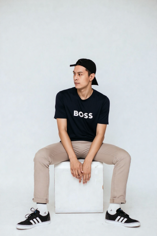 Man wearing a black 'BOSS' t-shirt sitting on a white cube against a white background