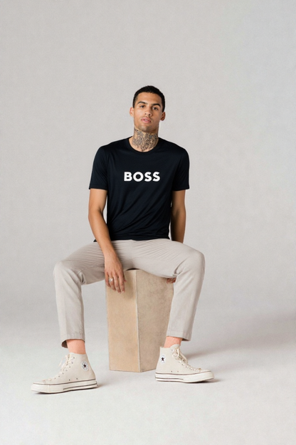 Person wearing a black 'BOSS' t-shirt sitting on a beige cube against a plain background